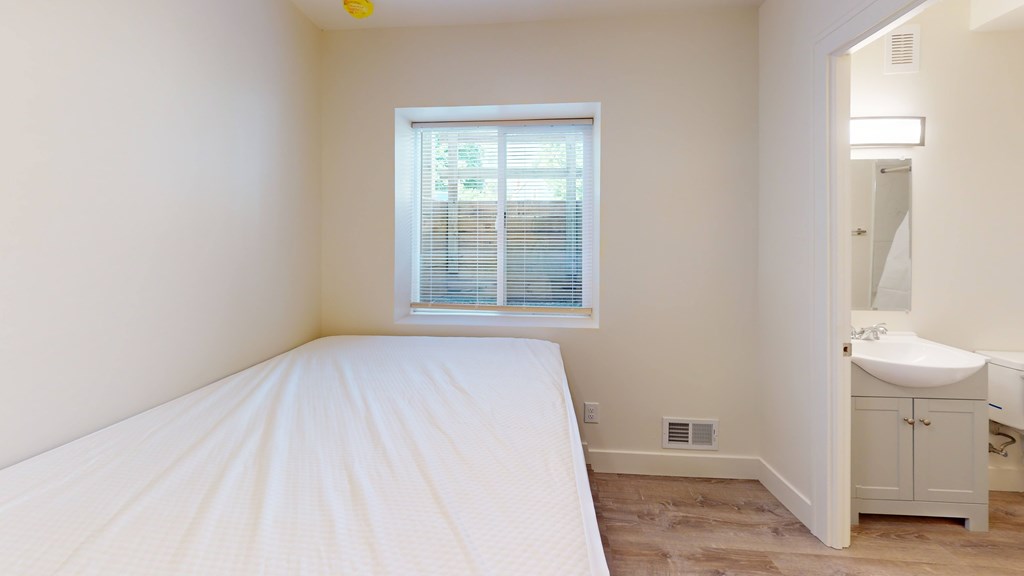 A white bedroom with a bed, sink, and window.